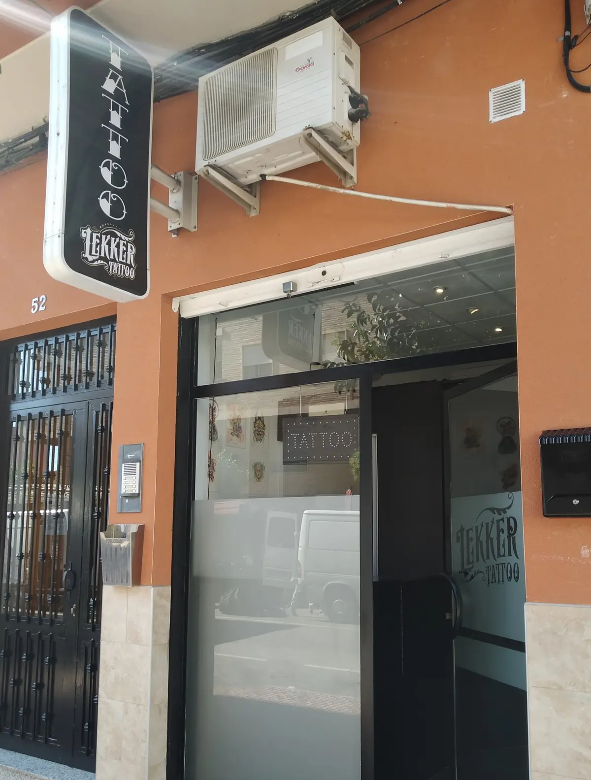 Fachada naranja de Lekker Tattoo en la Av. Juan Carlos I, 52, con el rótulo vertical de TATTOO